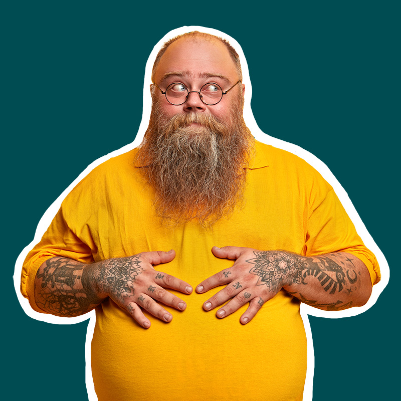 Isomahainen miesoletettu katsoo muikeasti partansa takaa oikealle. Hänen tatuoidut kätensä lepäävät mahan päällä. Päällään hänellä on keltainen paitapusero. 